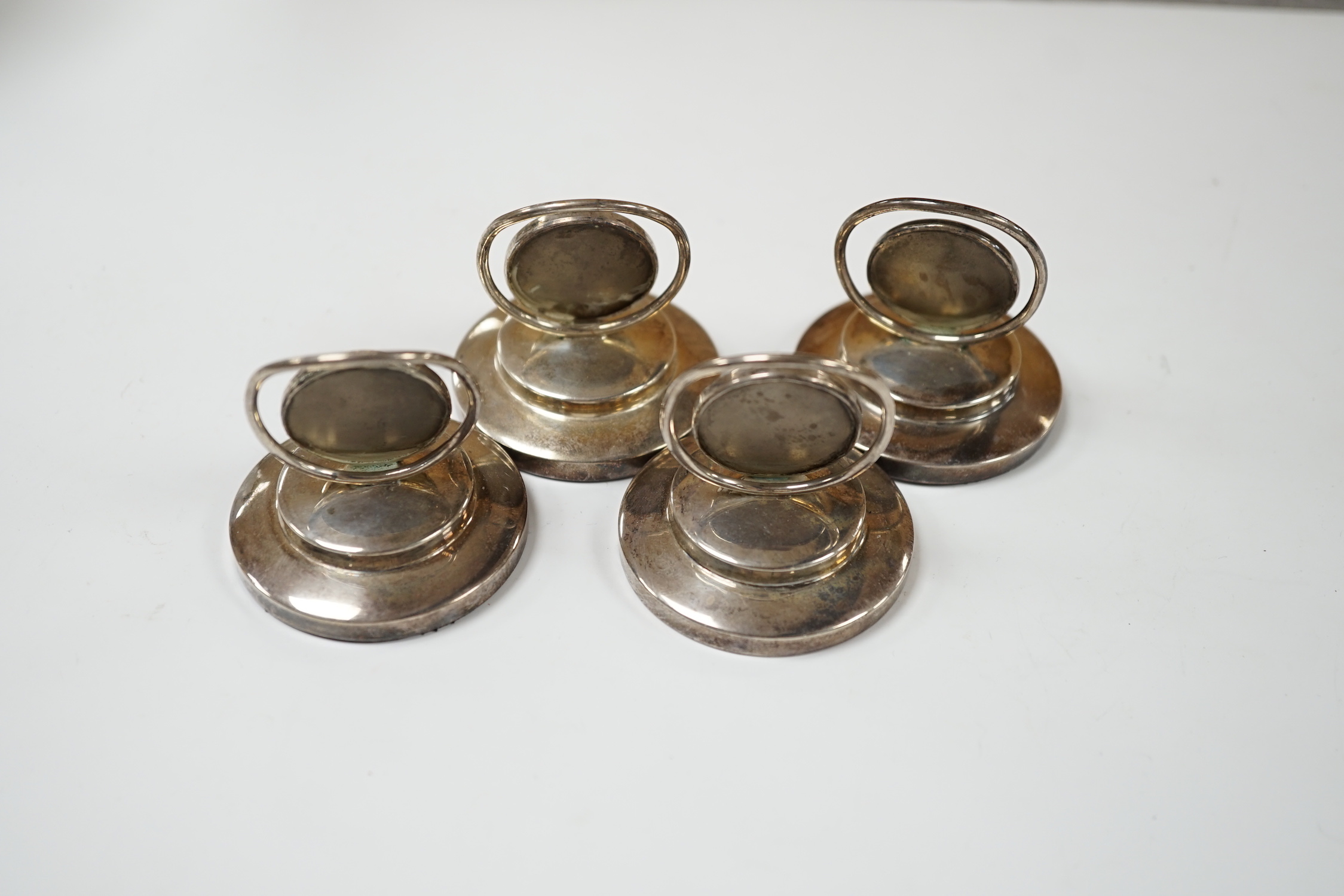 A set of four George V silver menu holders, each with inset painted panel of a wild bird, Adie Bros. Ltd, Birmingham, 1926, base diameter 5cm.